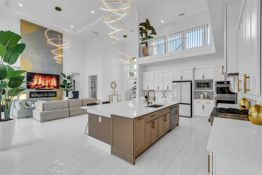 Kitchen Overlook: A chef’s island kitchen finished with sleek cabinetry, quartz counters, and professional appliances opens seamlessly to the soaring great room. Designer lighting and expansive sightlines connect cooking, dining, and entertaining in a space that balances modern elegance with everyday function.