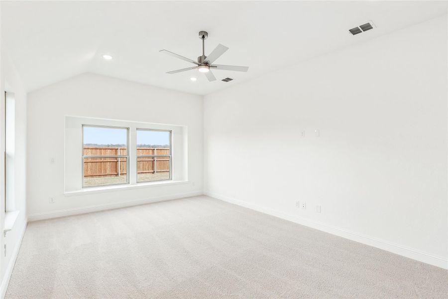 Empty bedroom with vaulted ceiling, ceiling fan, carpet flooring, and double windows overlooking a wood fence yard. Empty bedroom with vaulted ceiling, ceiling fan, carpet flooring, and double windows overlooking a wood fence yard.