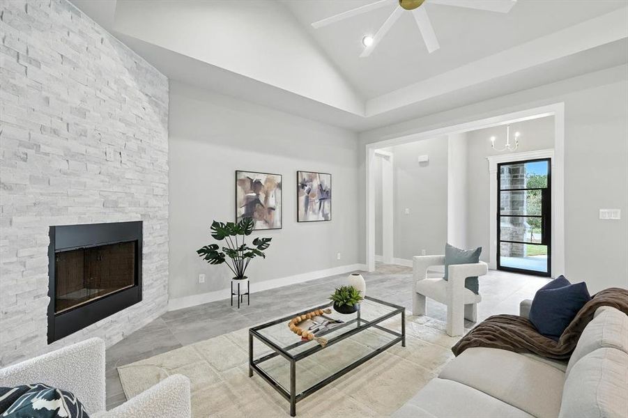 Tiled living room with a stone fireplace, vaulted ceiling, a ceiling fan, and a chandelier