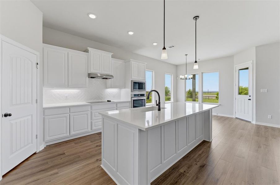 Kitchen featuring white cabinetry, a kitchen island with sink, light wood finished floors, tasteful backsplash, and stainless steel oven Kitchen featuring white cabinetry, a kitchen island with sink, light wood finished floors, tasteful backsplash, and stainless steel oven