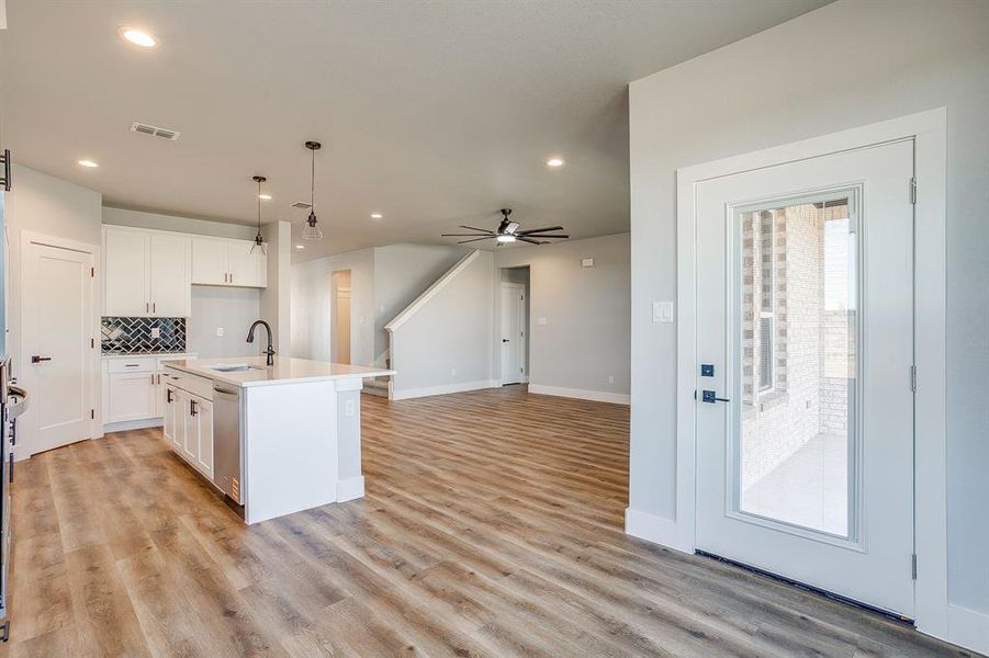 Kitchen featuring a kitchen island with sink, hanging light fixtures, backsplash, white cabinets, and light wood-type flooring