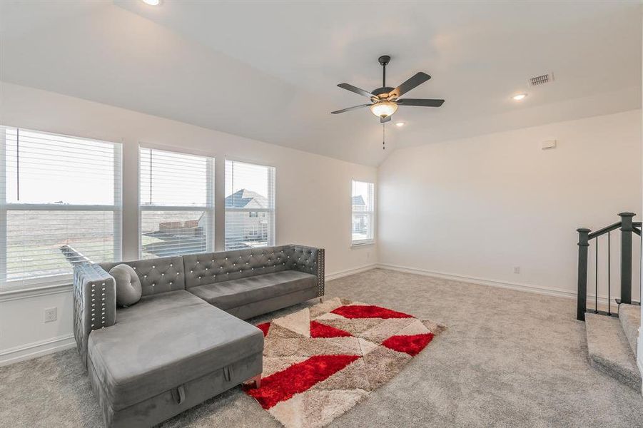 Carpeted living room featuring ceiling fan and vaulted ceiling