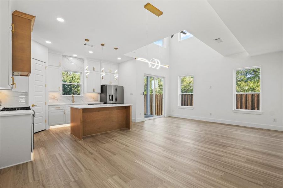 Kitchen with brown cabinets, open floor plan, hanging light fixtures, white cabinets, and light wood-style flooring