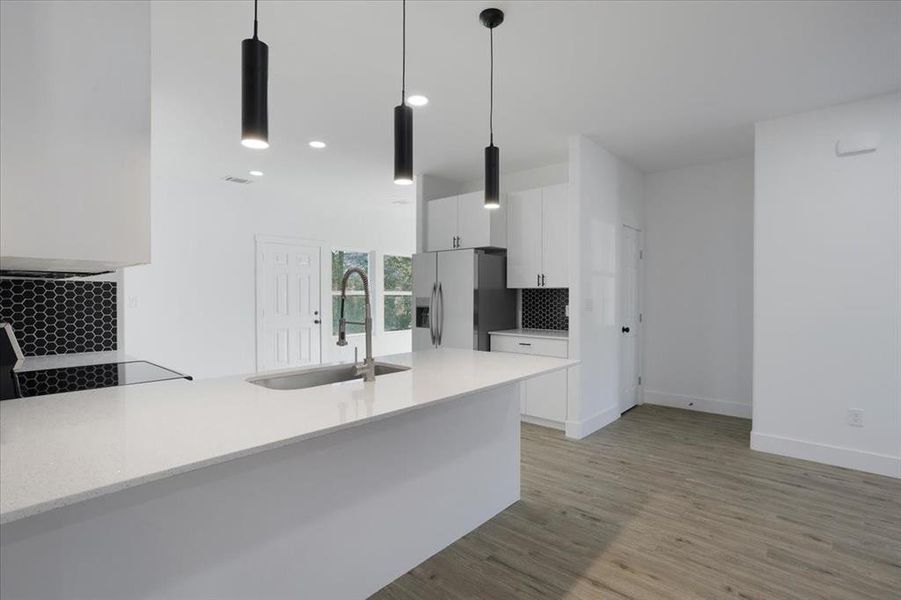 Kitchen with stainless steel fridge, sink, decorative light fixtures, light hardwood / wood-style floors, and white cabinetry