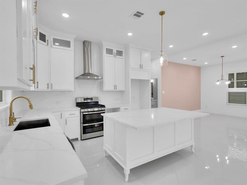 Kitchen featuring a center island, white cabinets, sink, gas stove, and wall chimney range hood