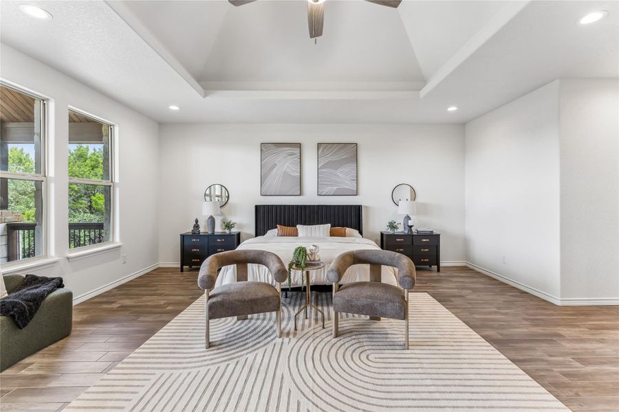A spacious primary bedroom features rich wood flooring, a decorative tray ceiling, and abundant natural light.