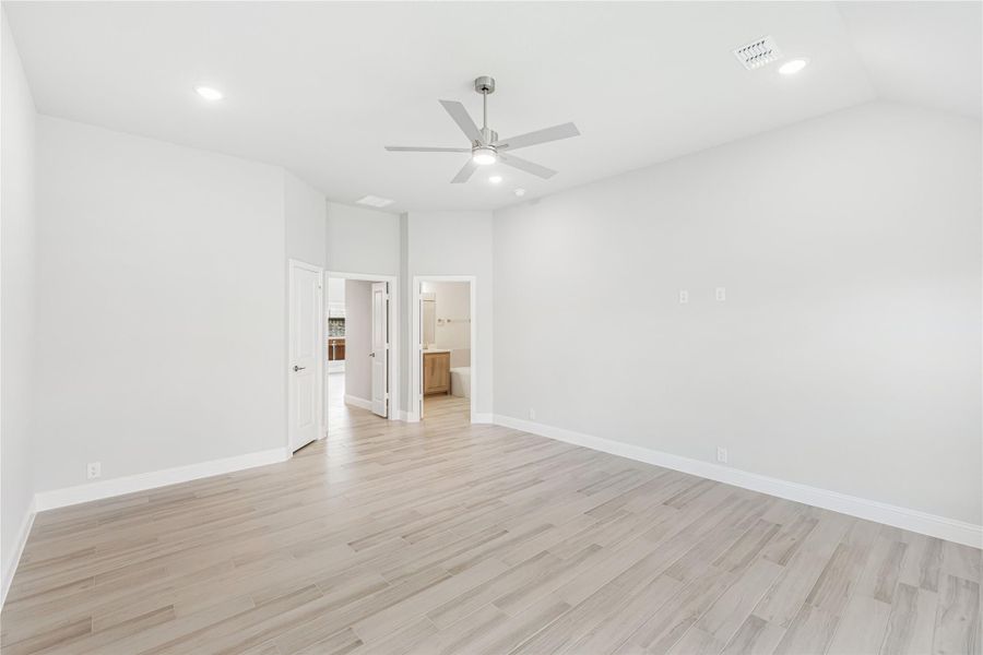 Empty bedroom with light wood floors, ceiling fan, and open ensuite bathroom doorway