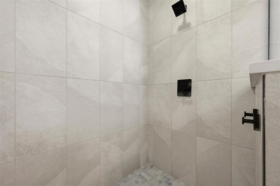 Primary Bathroom features large-format tile surround accented by a built-in niche. Walk-in shower includes rain shower head, handheld fixture, and black plumbing fixtures. Tile flooring extends throughout.