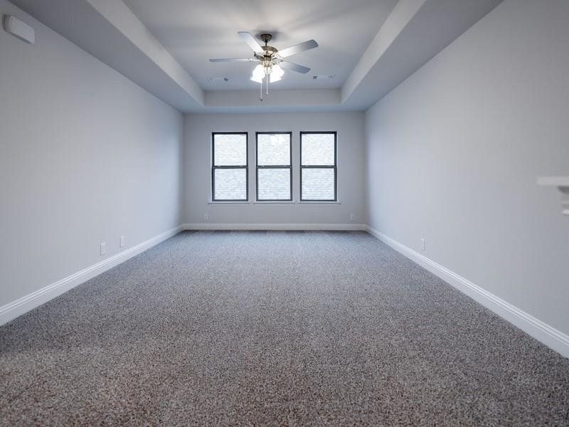 Carpeted spare room featuring ceiling fan and a tray ceiling