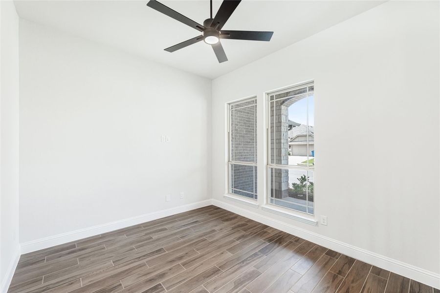 Empty room with wood-look tile floors, ceiling fan, and two windows with neighborhood view Empty room with wood-look tile floors, ceiling fan, and two windows with neighborhood view