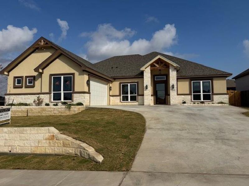 View of front of house with stone siding, concrete driveway, stucco siding, and a front lawn