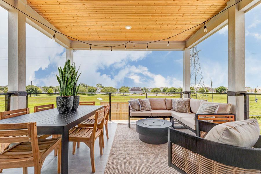 This covered outdoor living space is designed for year-round enjoyment, featuring a spacious seating area and dedicated dining space under a beautifully finished wood ceiling. String lighting adds a warm ambiance, while the open views create a tranquil setting. Perfect for entertaining or unwinding, this patio blends comfort and style effortlessly. The picture shown is from the model home with the same floor plan, Rev floor plan.