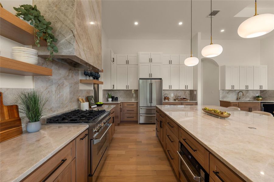 Two tone kitchen with open shelves, high end appliances, two tone color scheme, decorative backsplash, and hanging light fixtures