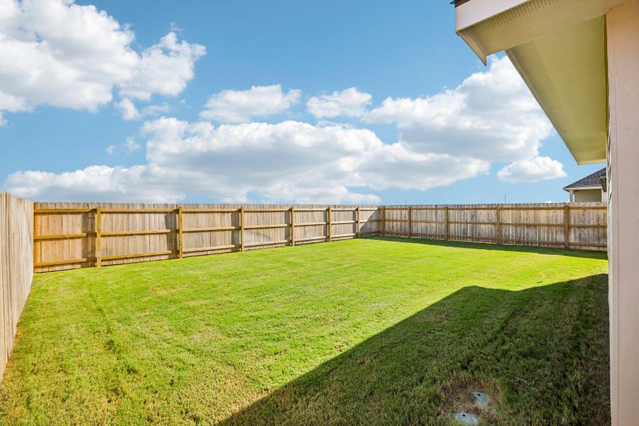 An expansive green lawn is fully enclosed by a sturdy wooden privacy fence under sunny skies.