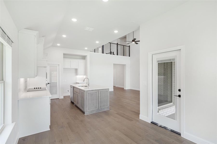 Open kitchen with gray island, white cabinets, hardwood floors, and high ceilings with upper-level railing visible