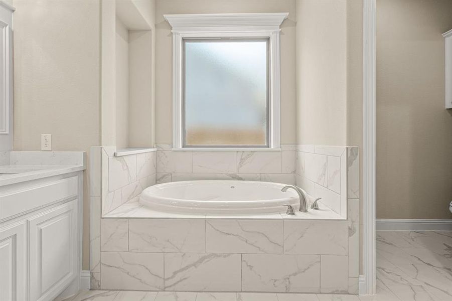 Bathroom with tiled tub, tile patterned flooring, and vanity