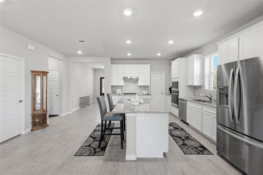 Kitchen featuring a central island with granite countertops, stainless steel appliances, white cabinetry, and recessed lighting