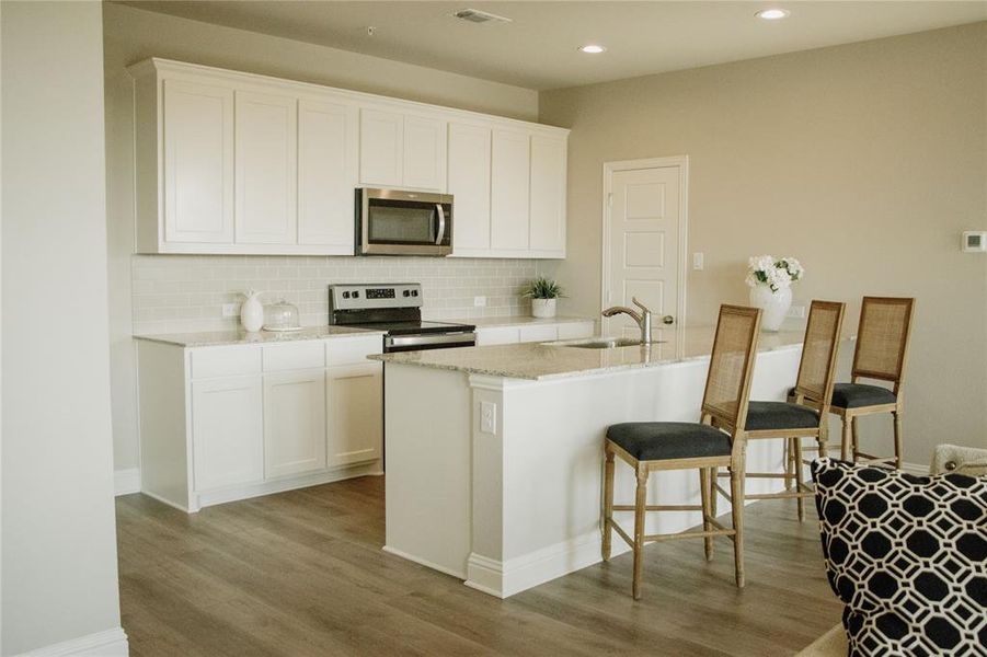 Kitchen with sink, white cabinets, a kitchen island with sink, stainless steel appliances, and light hardwood / wood-style flooring