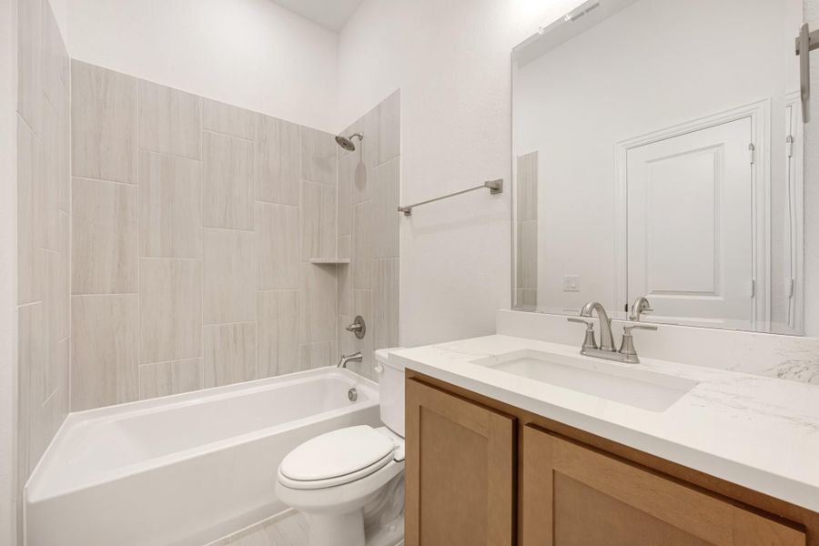 Bathroom with tiled tub-shower combo, wood vanity with white countertop, and toilet