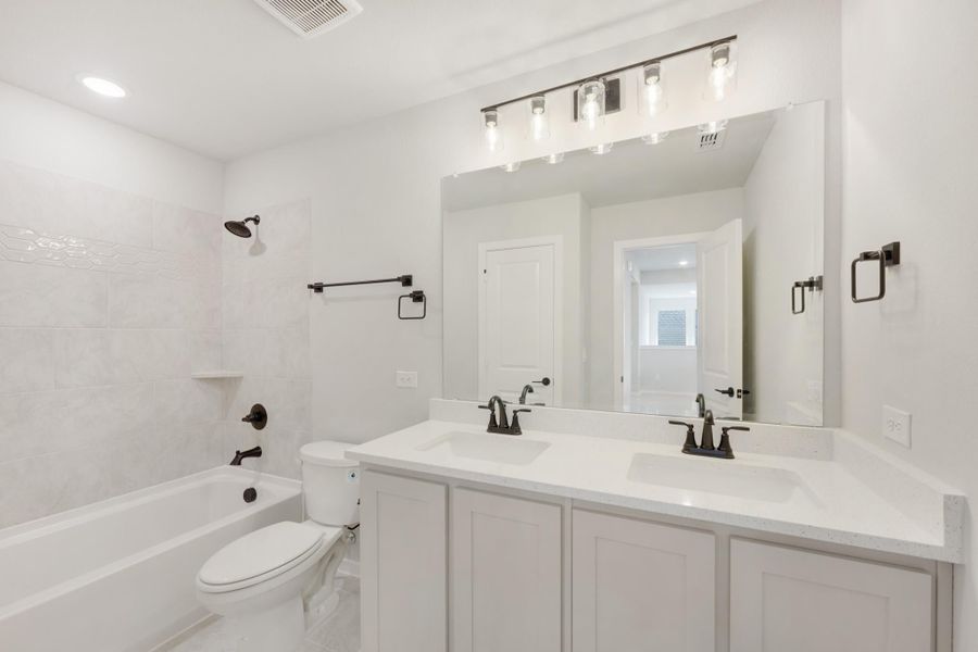 Bathroom with double sink vanity, white cabinets, tiled tub-shower combo, and large mirror with light bar above