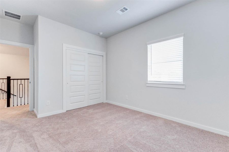 A cozy secondary bedroom upstairs features soft carpeting, a large window, and a double-door closet for added storage. Its location just off the game room makes it ideal for a flexible guest room, study, or creative space.