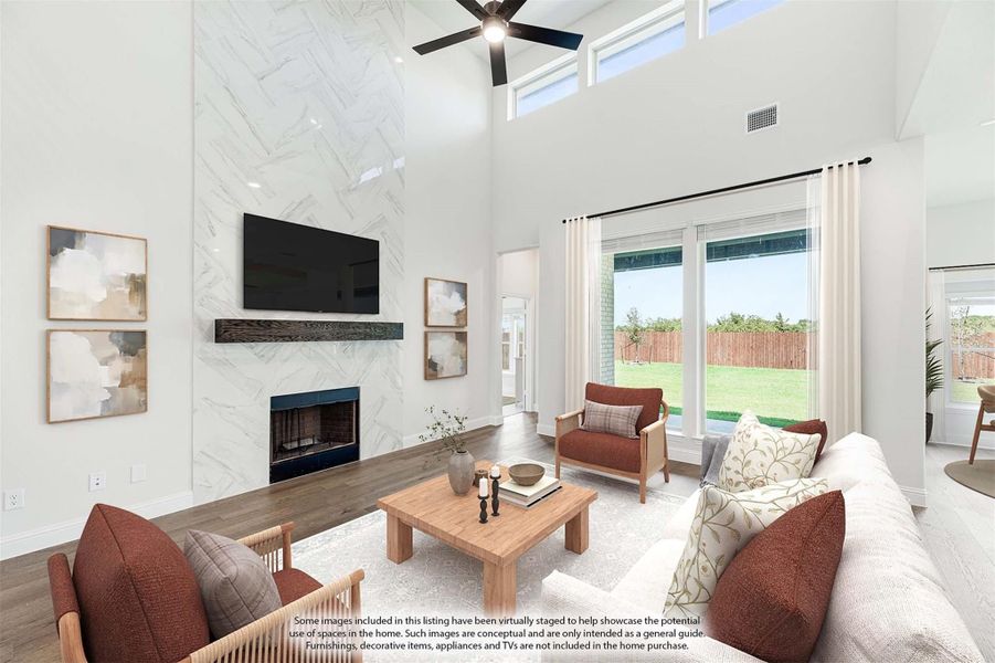 Living room with two-story marble fireplace wall, ceiling fan, mounted TV, and large windows overlooking backyard
