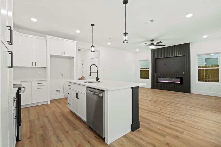 Kitchen featuring open floor plan, white cabinets, stainless steel dishwasher, and hanging light fixtures