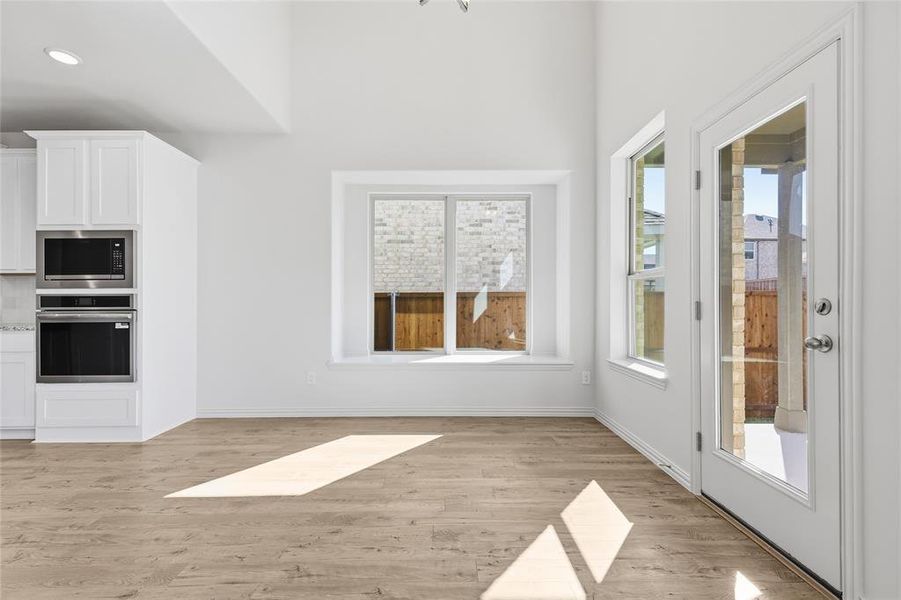 Kitchen with white cabinets, stainless steel appliances, light wood-type flooring, and light stone counters