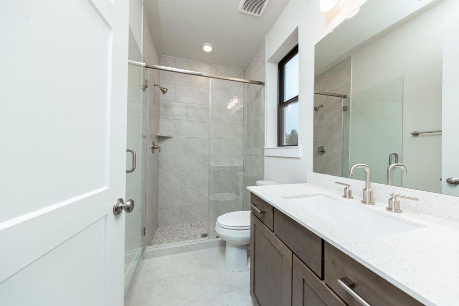 The private en suite bathroom features a modern white vanity with brushed nickel fixtures, mirror, lights, recessed lighting over the walk-in shower.