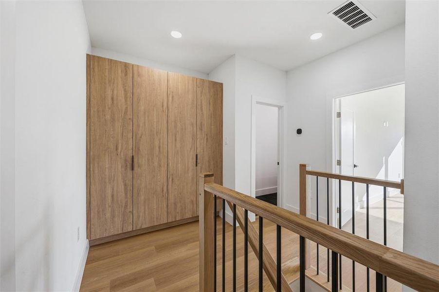 Staircase Landing features recessed lighting. Built-in wood storage cabinets maximize functionality. Wood and black metal railing lines the landing area. Vinyl flooring extends throughout.