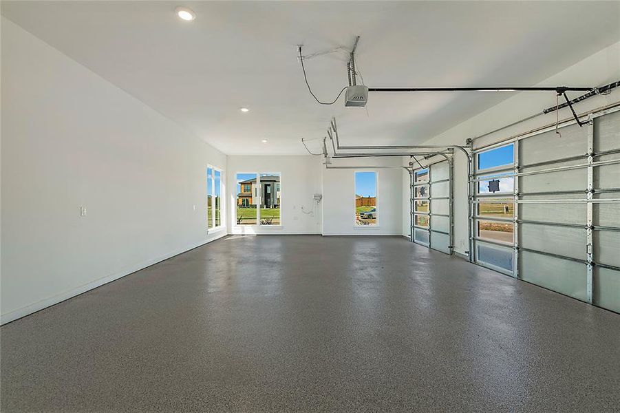 Spacious multi-car garage featuring an epoxy-coated concrete floor, two glass-paneled garage doors with automatic openers, and recessed ceiling lighting Spacious multi-car garage featuring an epoxy-coated concrete floor, two glass-paneled garage doors with automatic openers, and recessed ceiling lighting