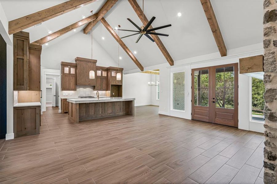 Unfurnished living room featuring high vaulted ceiling, beam ceiling, french doors, light wood-style floors, and a ceiling fan Unfurnished living room featuring high vaulted ceiling, beam ceiling, french doors, light wood-style floors, and a ceiling fan