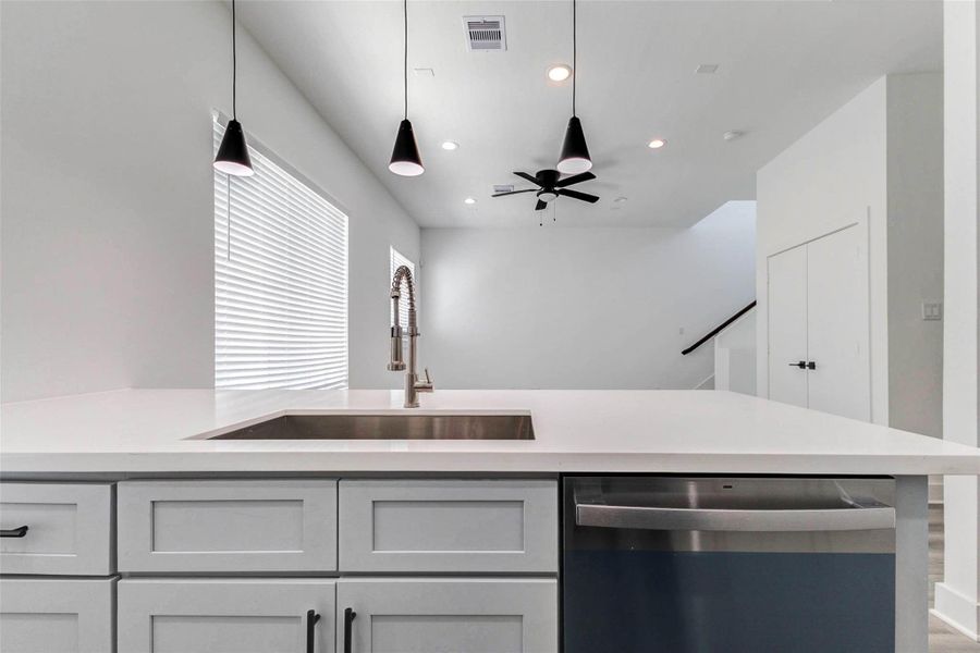 The expansive kitchen island creates a natural gathering place with a sleek quartz-style surface, undermount sink, professional-style faucet, stainless steel dishwasher, and generous storage. Three modern pendant lights illuminate the workspace while the open design maintains a seamless connection to the adjoining living area. The expansive kitchen island creates a natural gathering place with a sleek quartz-style surface, undermount sink, professional-style faucet, stainless steel dishwasher, and generous storage. Three modern pendant lights illuminate the workspace while the open design maintains a seamless connection to the adjoining living area.