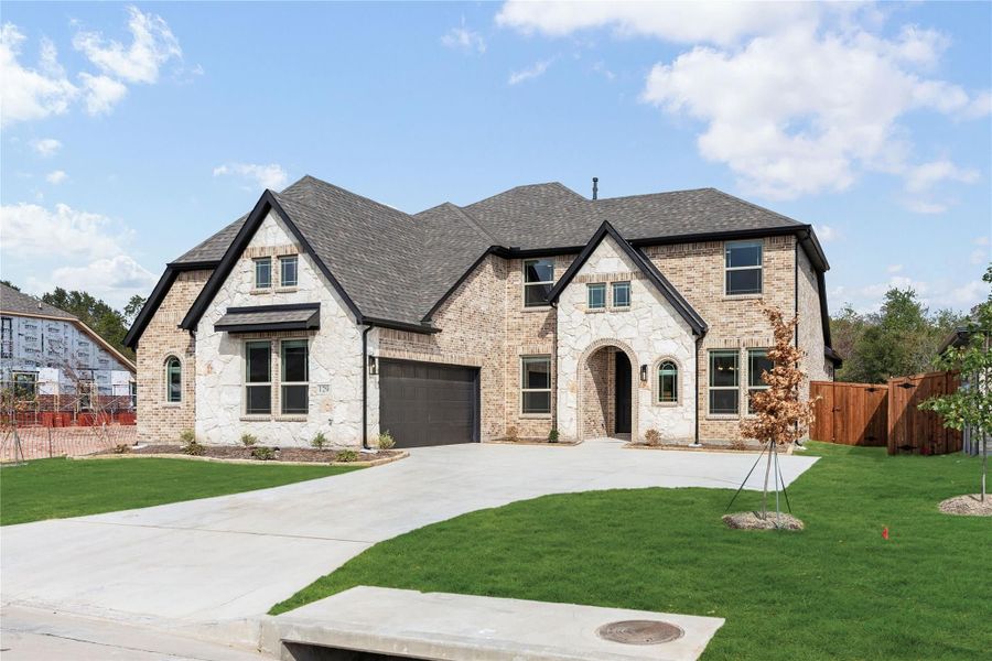 Two-story home with brick and stone exterior, two-car garage, arched entry, and green front lawn