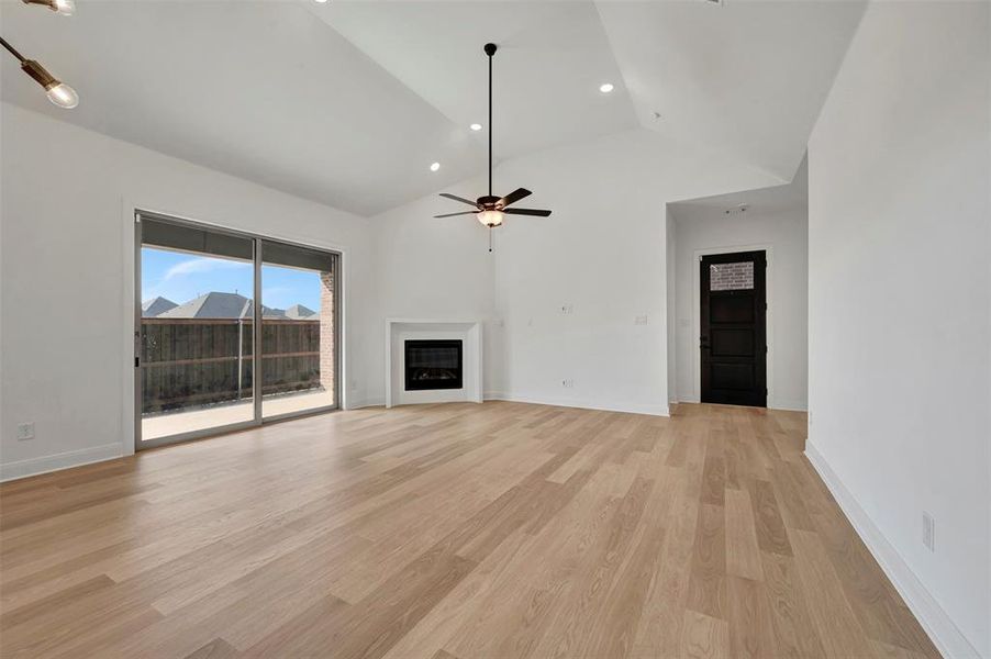 Unfurnished living room with a fireplace, light wood finished floors, lofted ceiling, recessed lighting, and ceiling fan Unfurnished living room with a fireplace, light wood finished floors, lofted ceiling, recessed lighting, and ceiling fan
