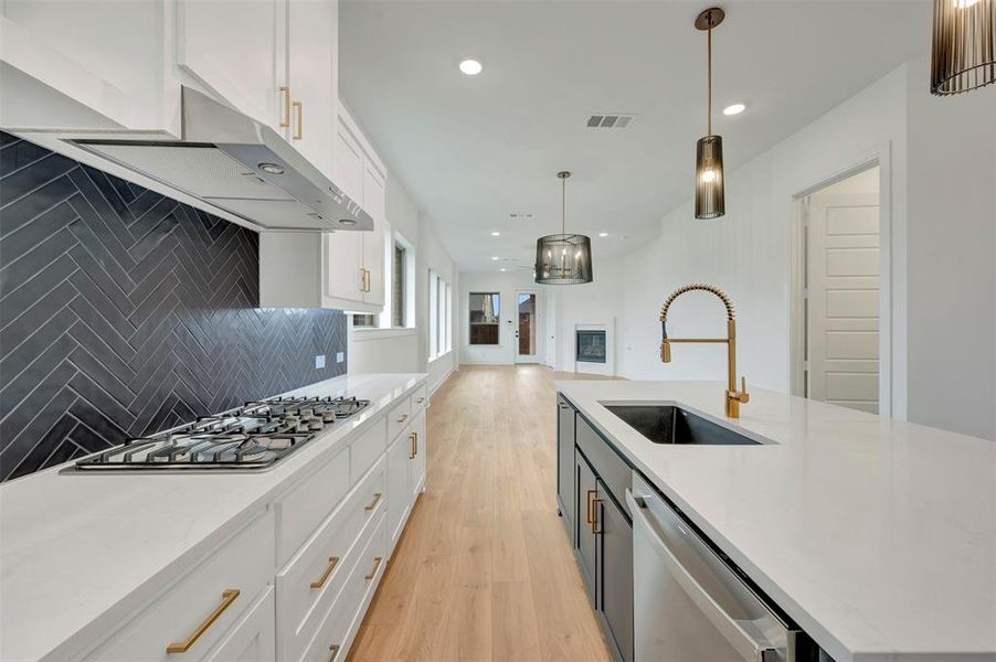 Modern kitchen featuring a gas range, herringbone tile backsplash, white cabinetry with brass hardware, and an island with a built-in sink and gold-tone faucet