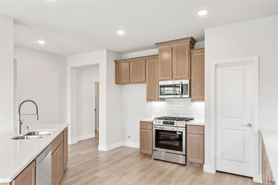 Kitchen with tan wood cabinets, stainless steel appliances, white countertops, and light hardwood floors