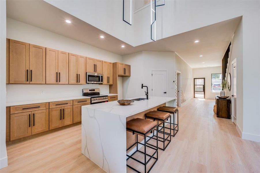 Kitchen featuring appliances with stainless steel finishes, light wood-type flooring, a breakfast bar, sink, and an island with sink