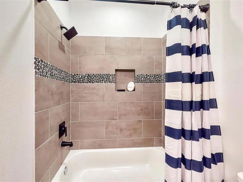 A modern bathroom with a white bathtub, a walk-in shower, and a vanity. The bathroom has white subway tiles with gray veining throughout. The walls are a light cream color, and the lighting is bright.