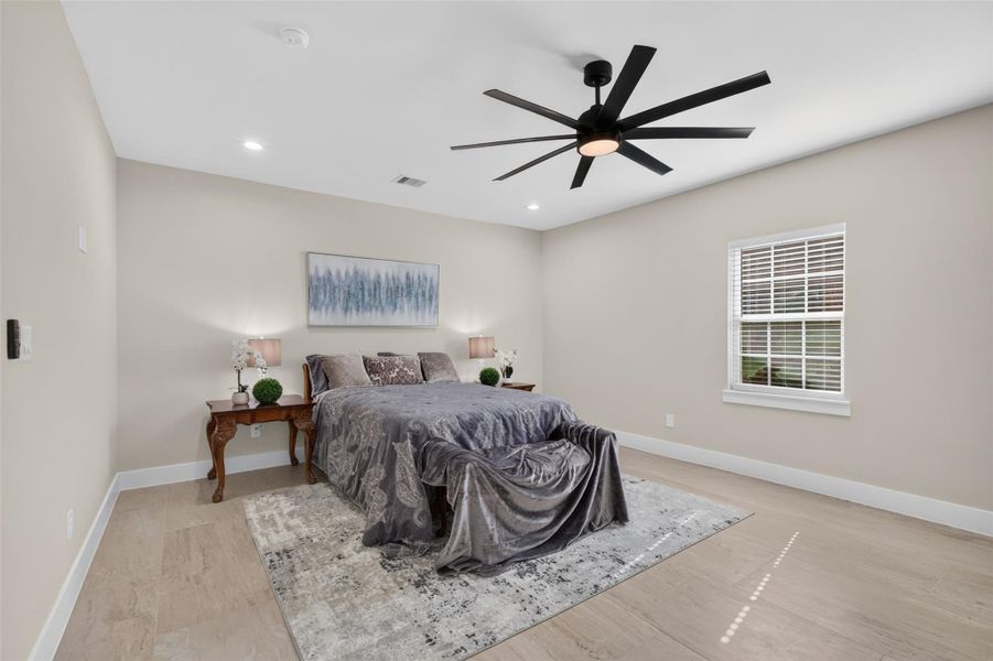 Spacious bedroom featuring a modern ceiling fan, ample natural light from a large window, and elegant decor with a cozy bed and matching side tables.