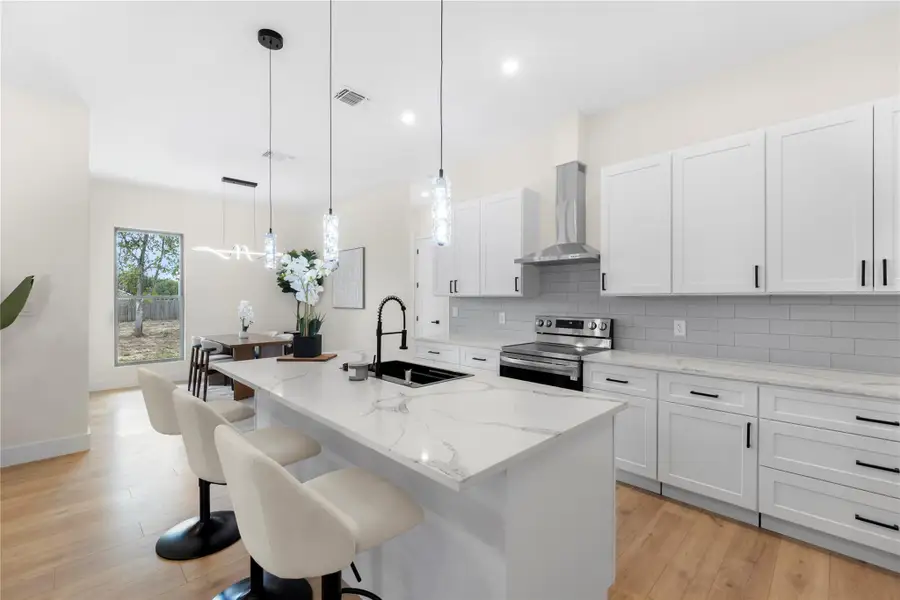 Kitchen with an island with sink, light stone counters, wall chimney exhaust hood, white cabinetry, and tasteful backsplash Kitchen with an island with sink, light stone counters, wall chimney exhaust hood, white cabinetry, and tasteful backsplash