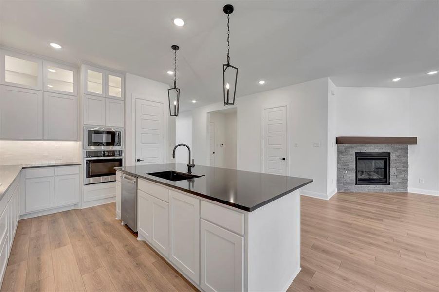 Kitchen featuring a center island with sink, glass fronted cabinets, pendant lighting, stainless steel appliances, and a fireplace