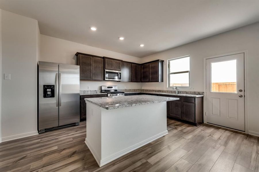 Kitchen featuring appliances with stainless steel finishes, hardwood / wood-style floors, a kitchen island, and dark brown cabinetry