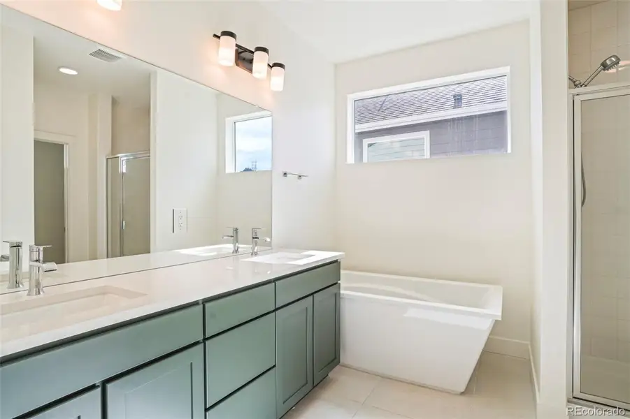 Bright and modern primary bathroom with dual vanity, quartz countertops, soaking tub, and walk-in shower in this newer construction home in Morrison Colorado