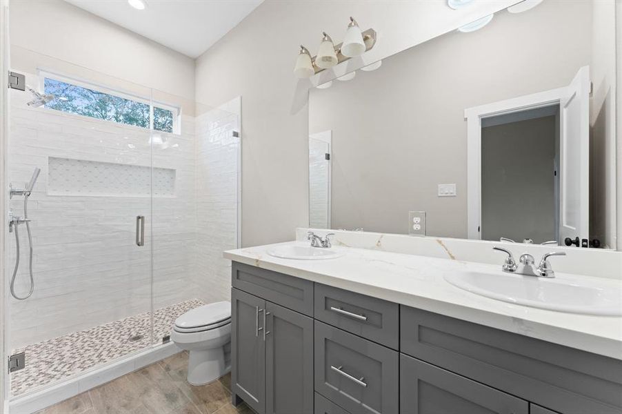 This modern bathroom features a spacious glass-enclosed shower, double sinks with a sleek countertop, and stylish gray cabinetry.