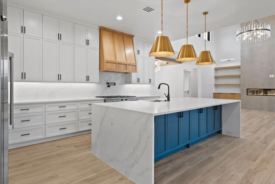 A gourmet kitchen boasts sleek white cabinetry, a waterfall island, and golden pendant lighting.