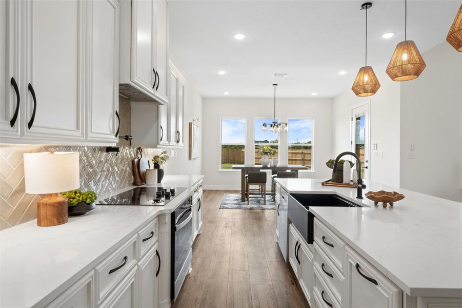 Kitchen with white cabinets, pendant lighting, an island with sink, dark wood finished floors, and light stone counters Kitchen with white cabinets, pendant lighting, an island with sink, dark wood finished floors, and light stone counters