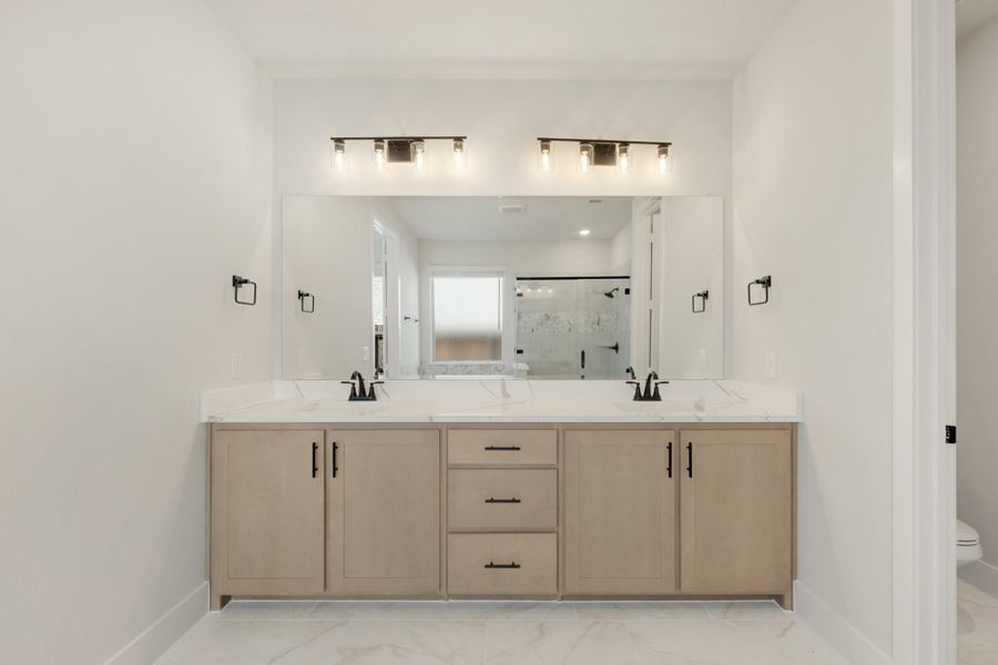Bathroom double vanity with light wood cabinets, white quartz countertop, dual sinks, and large mirror with overhead lighting.