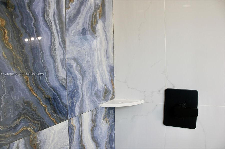 Large-format blue and gold veined accent tile, solid white wall tile, matte black square shower control handle, and corner mounted shelf