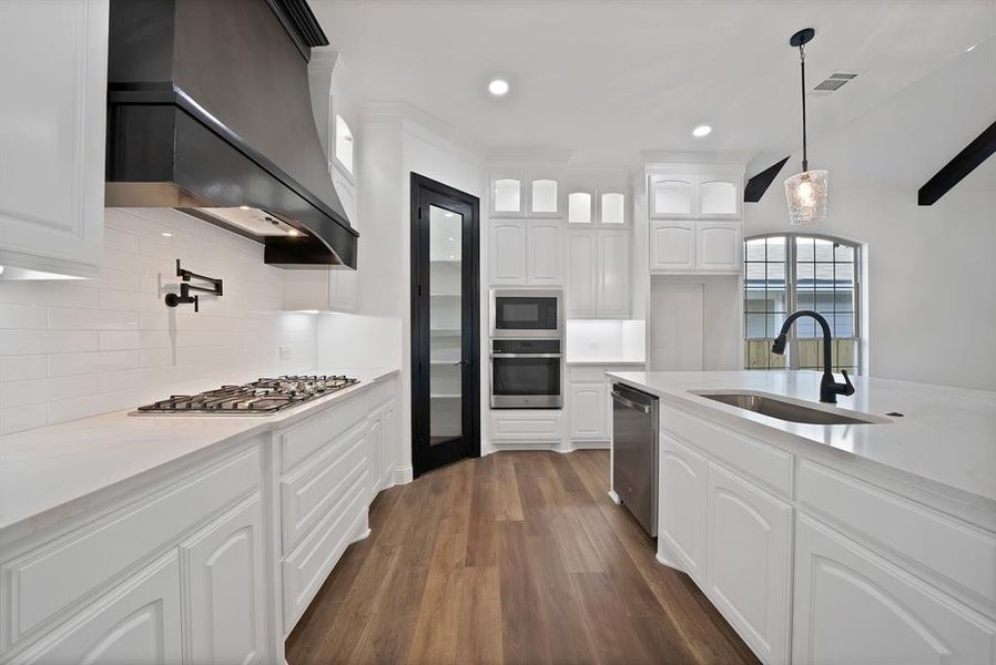 Kitchen with white cabinets, custom exhaust hood, dark wood-type flooring, appliances with stainless steel finishes, and backsplash